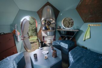 intérieur conker gris bleu, aménagé en bar lounge, table basse prêt pour les invités, porte ovale ouverte, mini coin cuisine, fauteuils en velours bleu