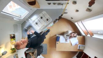 photo prise de haut, où l'on voit Jan Korbes et sa fille Liuka installés dans la cuisine du rdc, Jan prépare le repas, et Liuka fait ses devoirs sur la table