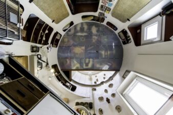 photo vue depuis la cuisine en rdv, vers le plafond et la chambre, dans la mini maison silo à grains, on y distingue la cuisine à l'envers à gauche, le mur d'escalade qui permet de monter dans la chambre, des rangements tout autour du silo à grains