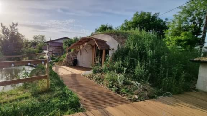 photo de la mini maison semi-enterrée scoophome appartenant à Jonathan Rollin à Choye, avec sa pièce d'eau devant. La maison est presque invisible, intégrée dans la végétation
