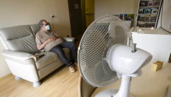 la photo montre une personne âgée enfermée chez elle en pleine canicule, assise dans son canapé, face à son ventilateur qui tourne à fond, triste image de parents qui sont le reflet de nous même demain