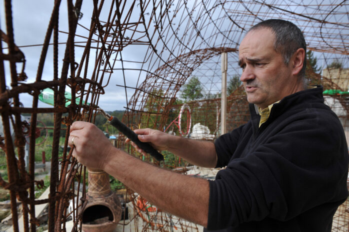 photo de moi, Philippe Delage, en plein ferraillage à la maison bulle de Montgivray, avec ma queue de cochon pour lier les liens deux boucles, avec en fond le ferraillage de la cuisine, mon brasero mexicain, et le chantier en général