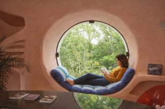 image ia grande fenêtre hublot maison bulle Joel Unal, adolescente en train de lire un livre, allongée dans le creux du hublot