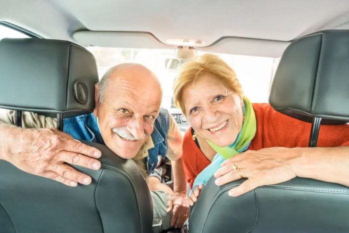 photo d'un couple de seniors assis dans leur camping car, prêts à partir à l'aventure ou en voyage, souriants et l'air heureux