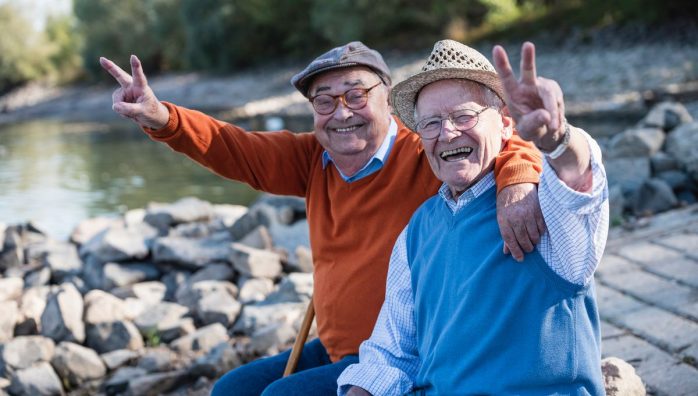 seniors copains heureux et souriants, se tenant pour l'épaule, surement en été avec leurs polos et leurs casquettes, au bord de l'eau